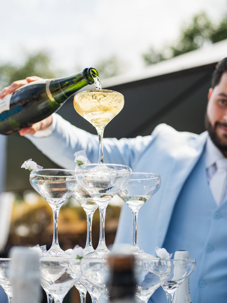 Champagne being poured into a tower of glasses at a stylish outdoor wedding celebration.